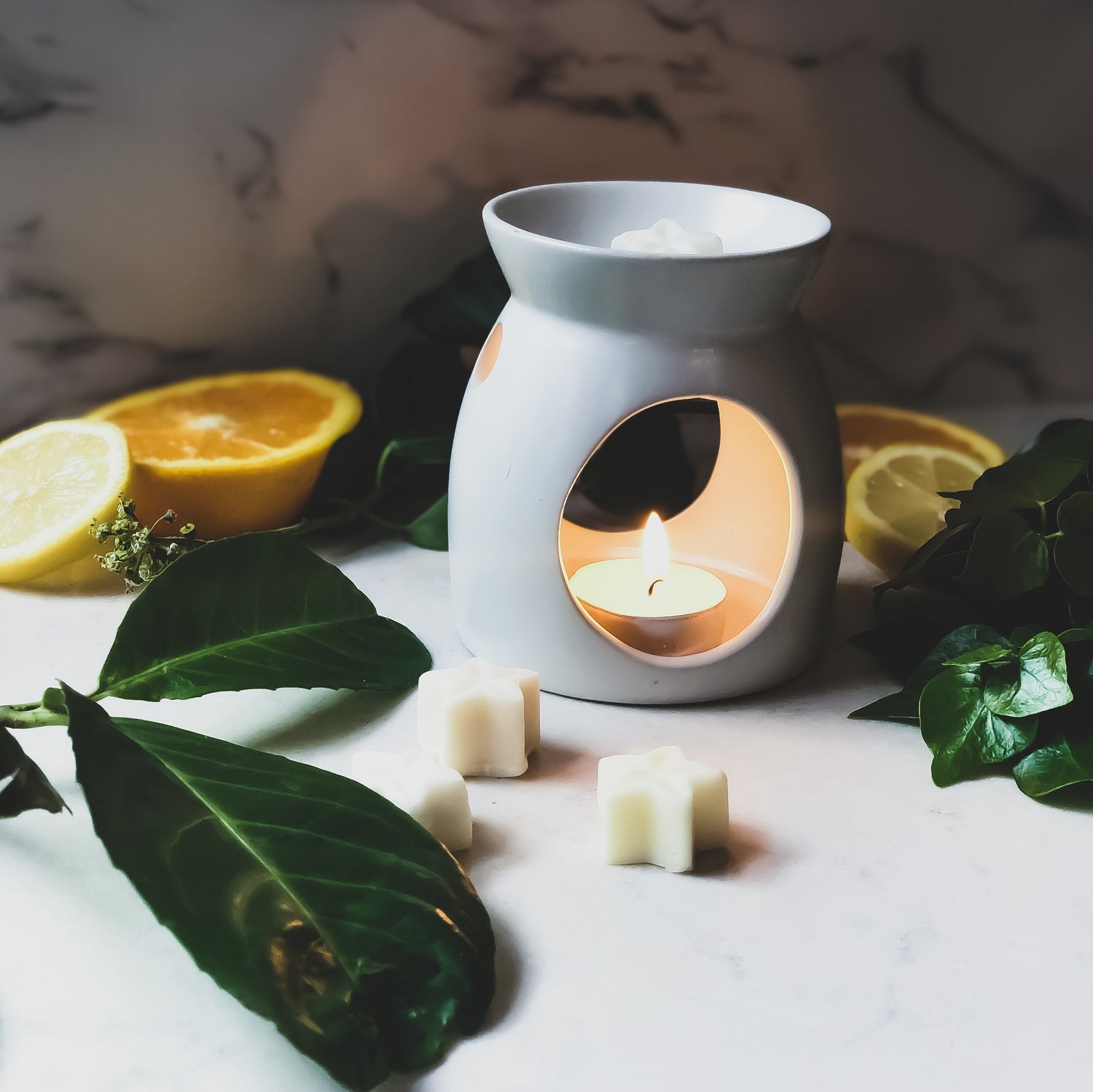 Star shaped wax melts being burnt in a wax burner, surrounded by fresh leaves and lemons