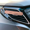 A stylish wooden car freshener, with Sage & Grace logo on it, clipped onto a car air vent